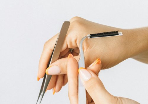 Close-up of hands using tweezers for eyelash extensions on white background.
