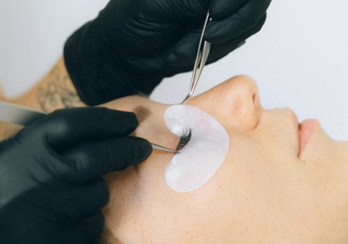 Close-up of a beautician applying eyelash extensions to a client in a salon setting.